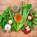 Disposition à plat d'herbes médicinales chinoises traditionnelles sur une surface en bois, comprenant de l'aloe vera, du gingembre, des baies de go...